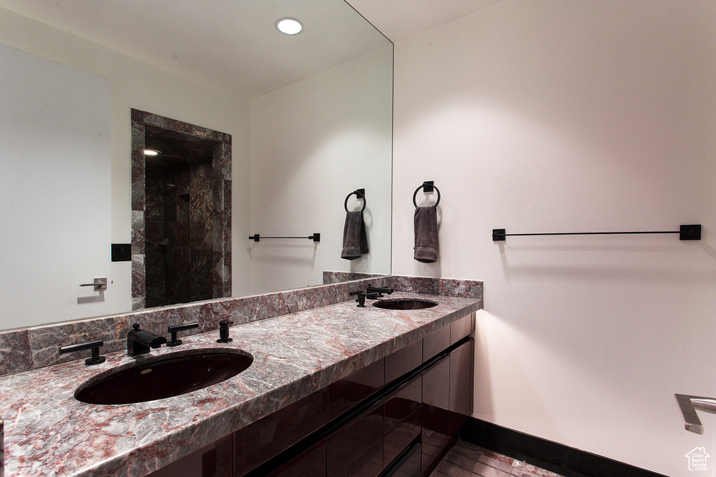 Bathroom featuring double vanity, tiled shower, recessed lighting, and baseboards