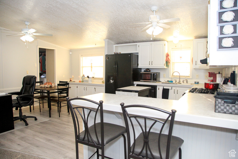 Kitchen featuring light wood-type flooring, a textured ceiling, white cabinets, kitchen peninsula, and black fridge with ice dispenser