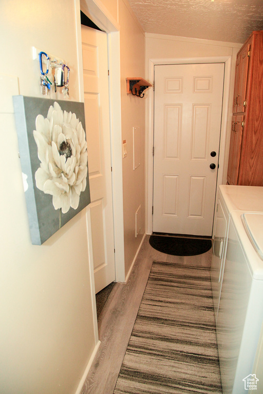 Doorway to outside featuring washing machine and clothes dryer, a textured ceiling, and hardwood / wood-style floors