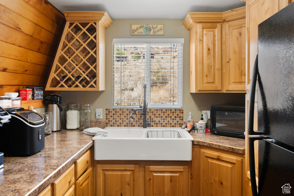 Kitchen with vaulted ceiling, backsplash, a fireplace, black refrigerator, and sink