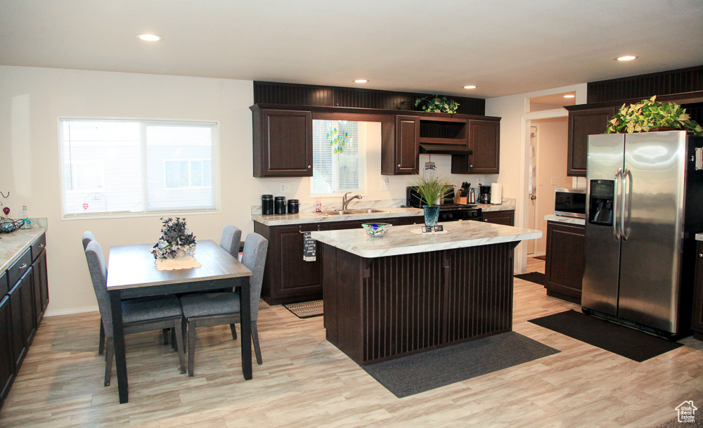 Kitchen with dark brown cabinets, stainless steel appliances, light hardwood / wood-style floors, and a center island