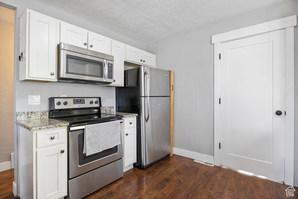 Kitchen featuring light stone counters, a textured ceiling, dark hardwood / wood-style floors, white cabinets, and stainless steel appliances