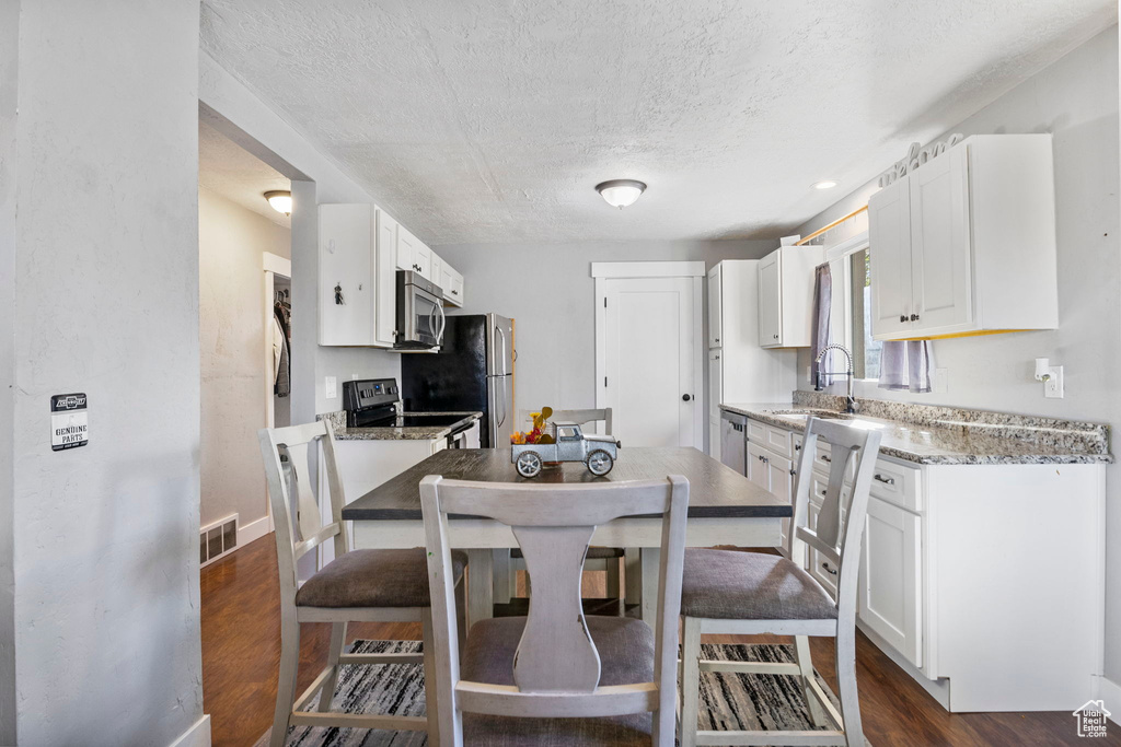 Kitchen with sink, a textured ceiling, white cabinetry, appliances with stainless steel finishes, and dark hardwood / wood-style floors