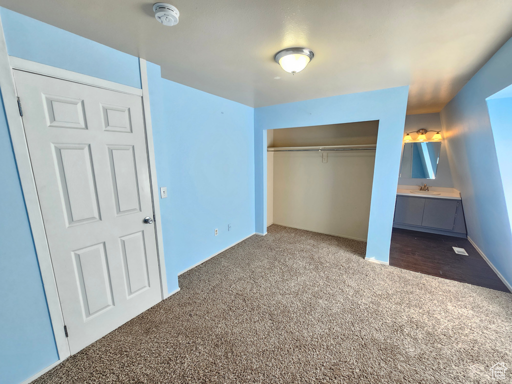 Unfurnished bedroom with sink, dark carpet, ensuite bath, and a closet