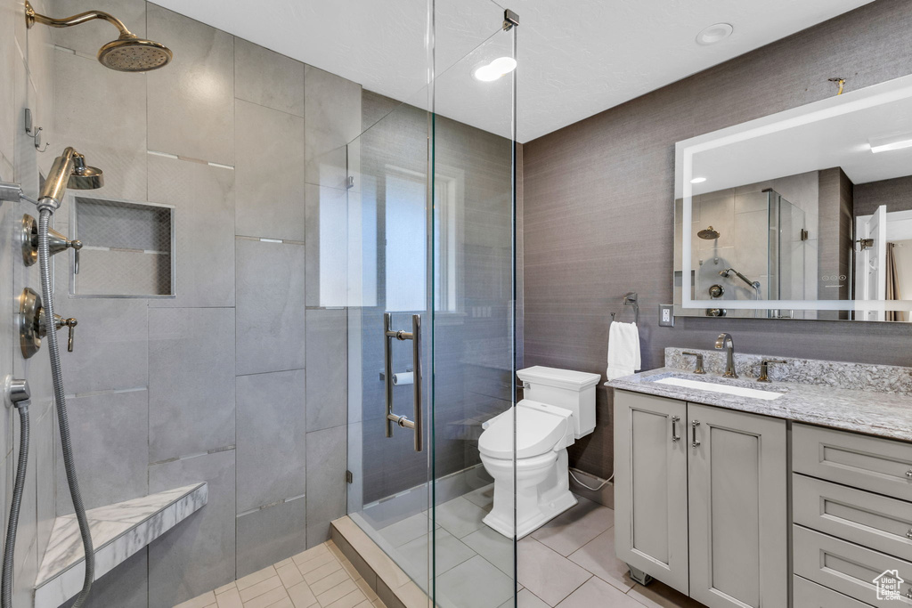 Bathroom with vanity, a shower with shower door, toilet, and tile patterned flooring