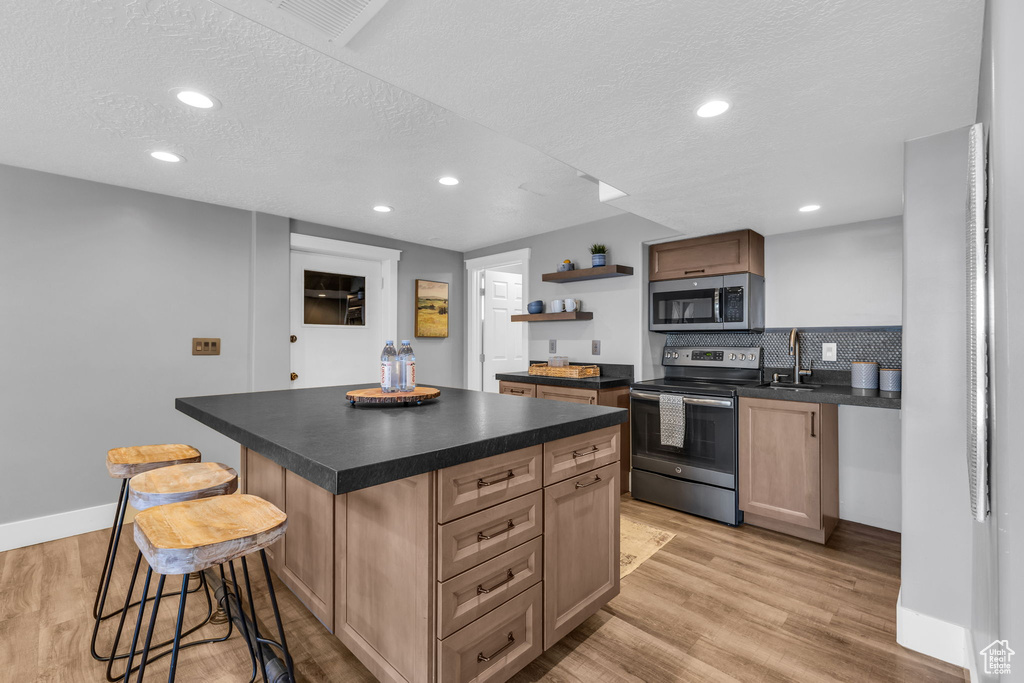 Kitchen featuring light hardwood / wood-style floors, a kitchen island, a textured ceiling, stainless steel appliances, and a kitchen bar