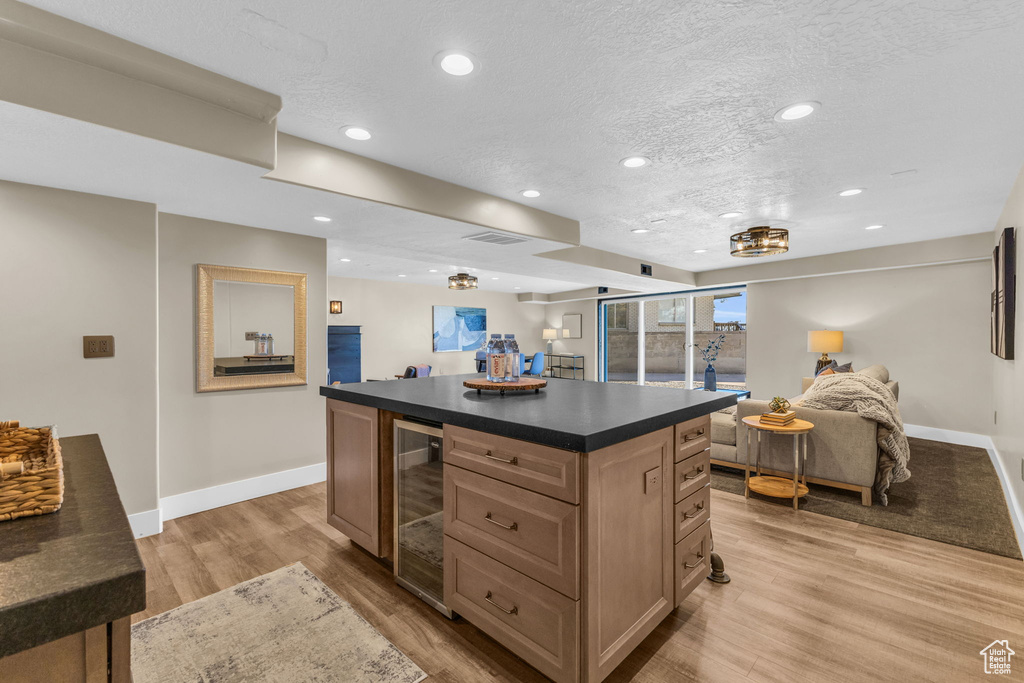 Kitchen with wine cooler, a kitchen island, a textured ceiling, built in desk, and light hardwood / wood-style floors