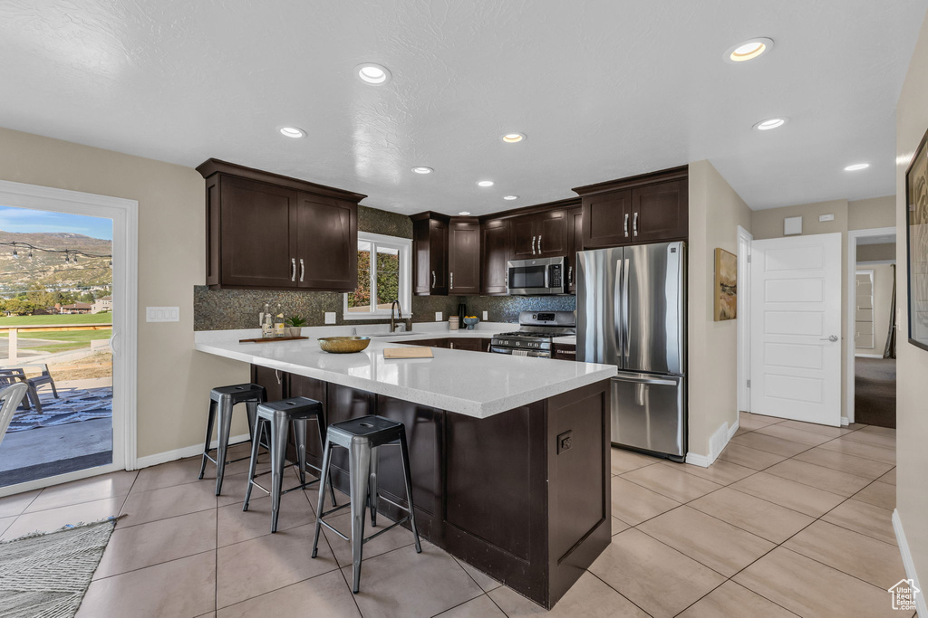 Kitchen featuring appliances with stainless steel finishes, backsplash, a kitchen bar, and light tile patterned floors