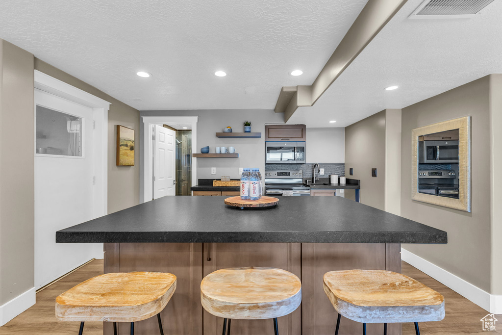 Kitchen with a textured ceiling, light hardwood / wood-style floors, a center island, and stainless steel appliances