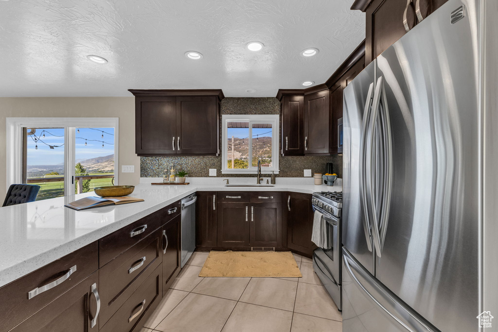 Kitchen featuring light stone countertops, light tile patterned floors, stainless steel appliances, a textured ceiling, and sink