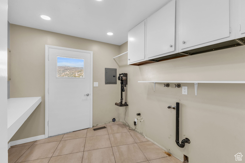 Washroom with electric panel, light tile patterned floors, hookup for a gas dryer, cabinets, and hookup for a washing machine