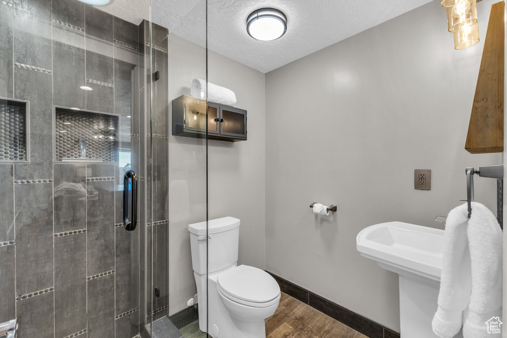 Bathroom featuring a textured ceiling, hardwood / wood-style floors, toilet, and an enclosed shower