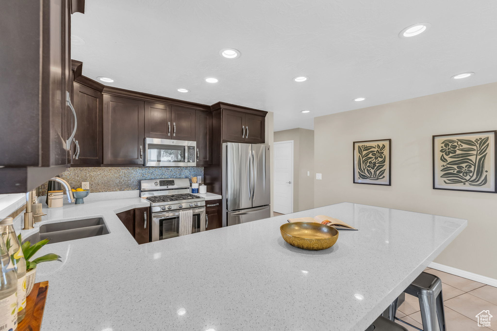 Kitchen with light stone countertops, stainless steel appliances, sink, and a breakfast bar area