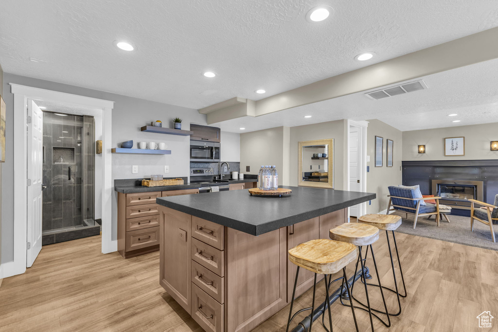 Kitchen with light wood-type flooring, a textured ceiling, a center island, and a breakfast bar