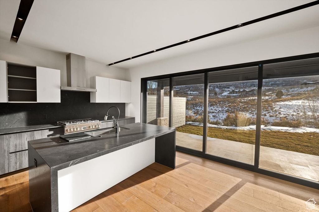 Kitchen featuring light hardwood / wood-style flooring, tasteful backsplash, stove, wall chimney exhaust hood, and white cabinets