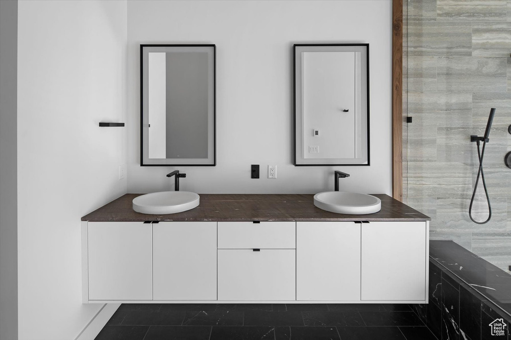 Bathroom featuring dual vanity, a tile shower, and tile flooring