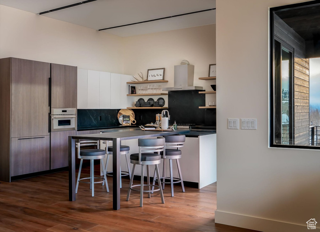 Kitchen with exhaust hood, backsplash, wood-type flooring, a breakfast bar, and stainless steel oven