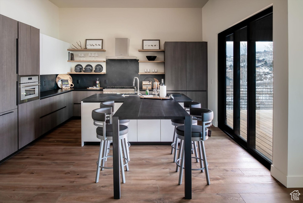 Kitchen featuring oven, a center island with sink, wall chimney exhaust hood, and light hardwood / wood-style flooring