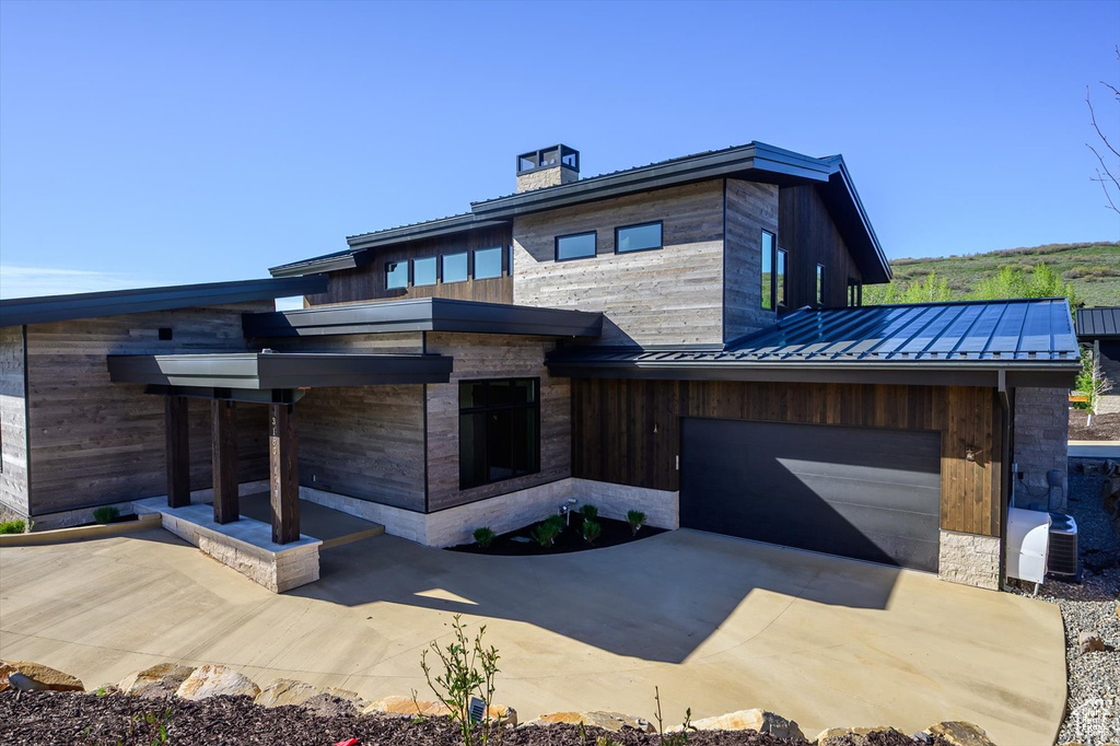 Modern home with a standing seam roof, metal roof, a chimney, driveway, and an attached garage