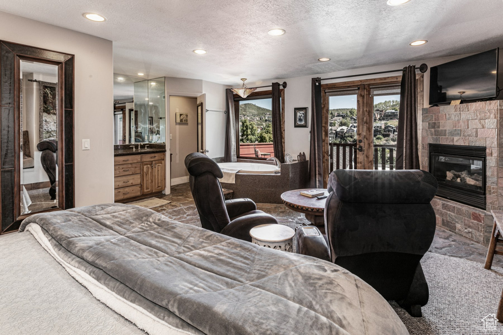 Carpeted bedroom with a textured ceiling, access to outside, sink, and ensuite bathroom