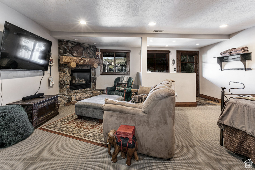 Carpeted living room featuring a textured ceiling and a stone fireplace