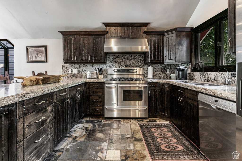 Kitchen featuring dark brown cabinetry, sink, appliances with stainless steel finishes, range hood, and vaulted ceiling