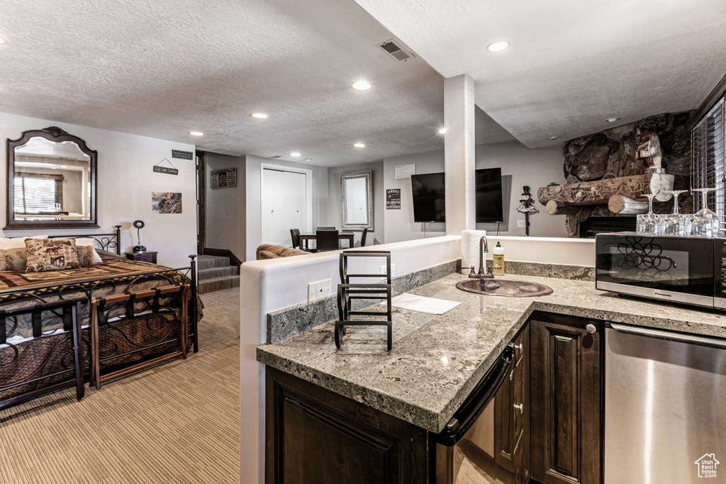 Kitchen featuring appliances with stainless steel finishes, a textured ceiling, dark brown cabinets, sink, and light carpet