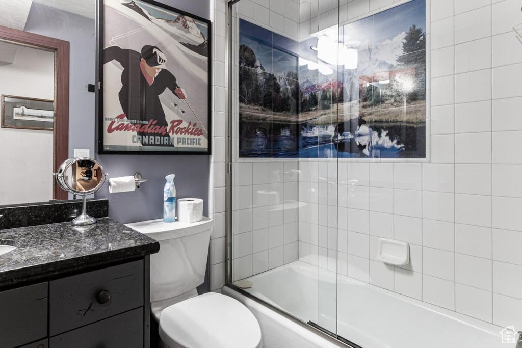 Full bathroom with bath / shower combo with glass door, vanity, and toilet