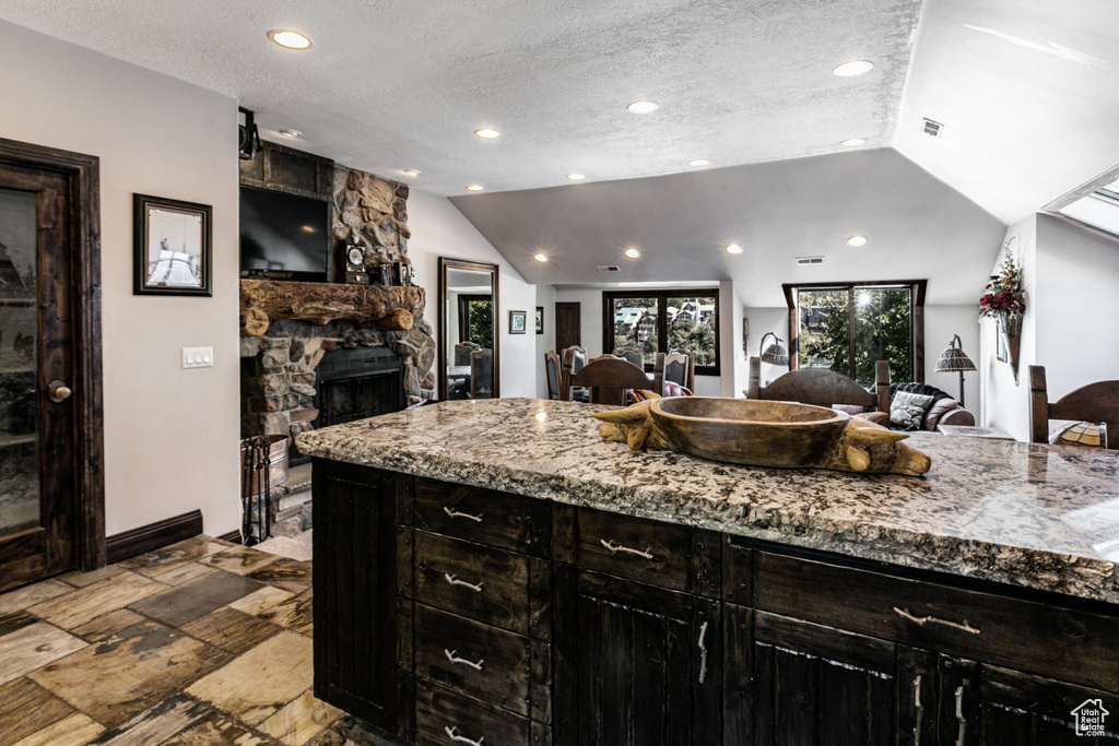 Kitchen featuring lofted ceiling, a textured ceiling, light stone counters, and a stone fireplace