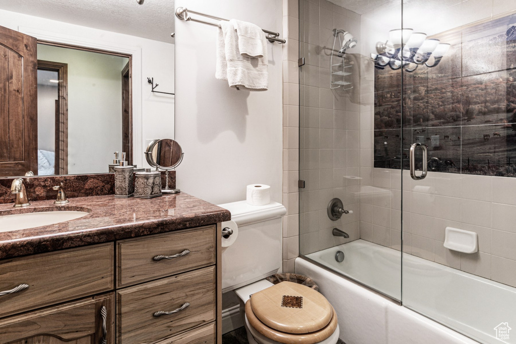 Full bathroom featuring a textured ceiling, combined bath / shower with glass door, vanity, and toilet