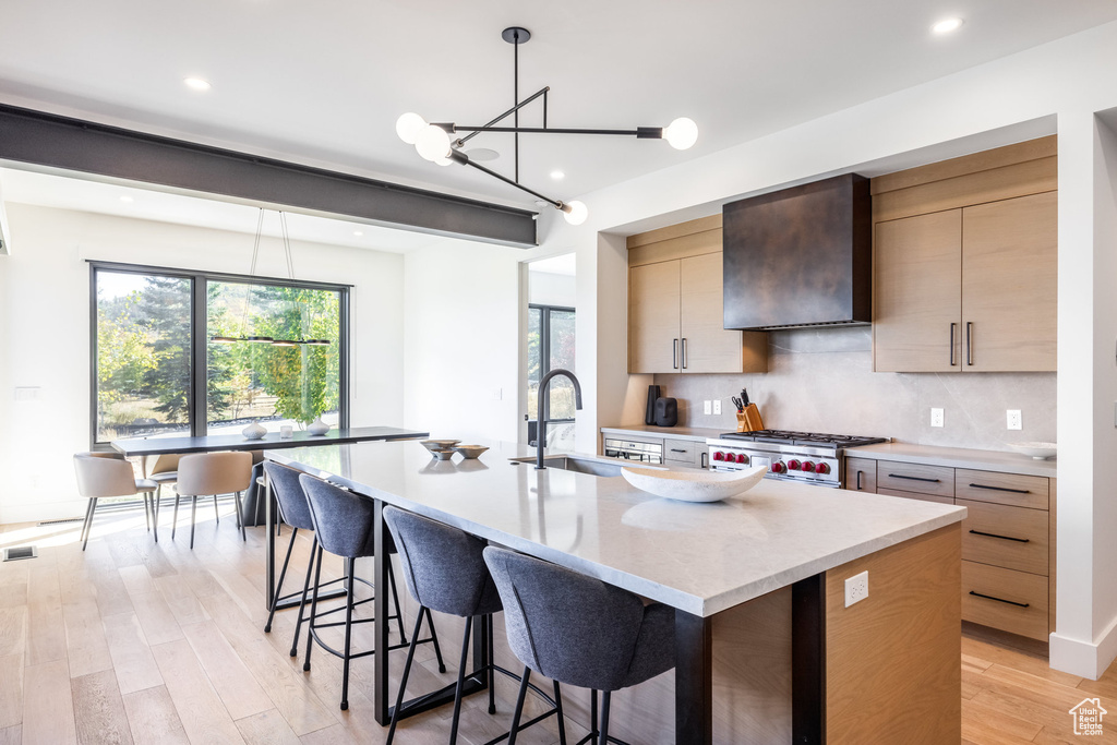 Kitchen featuring stove, backsplash, sink, wall chimney exhaust hood, and an island with sink