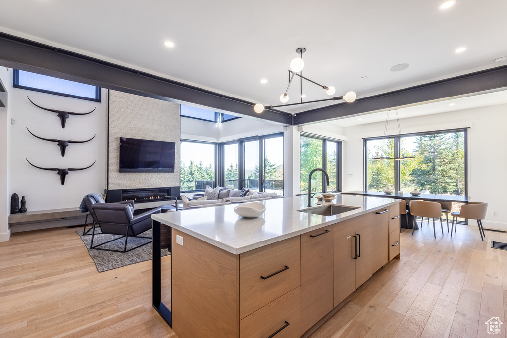 Kitchen with sink, light wood-type flooring, a fireplace, an island with sink, and a chandelier
