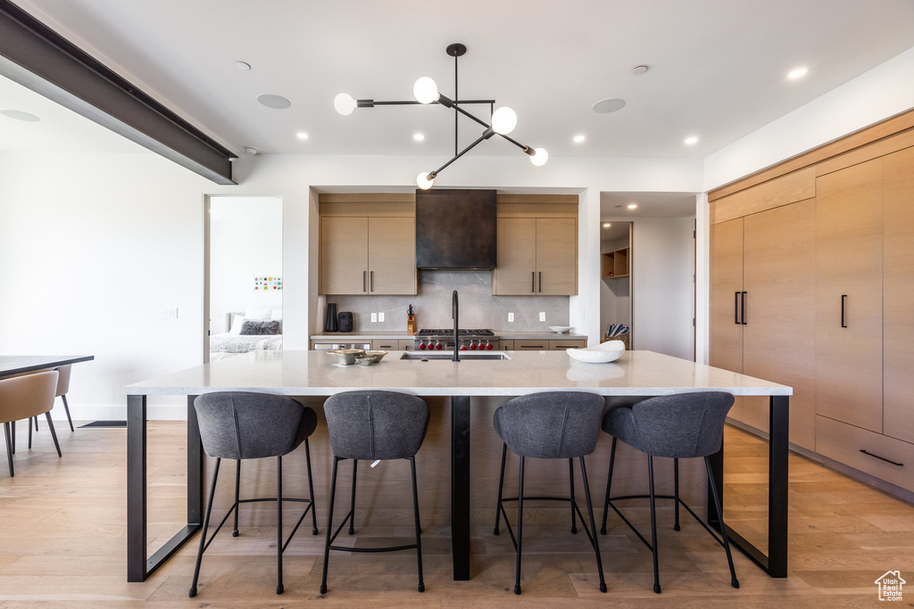Kitchen featuring hanging light fixtures, light hardwood / wood-style flooring, premium range hood, backsplash, and a breakfast bar area