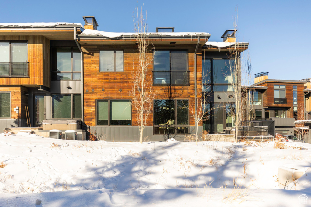 Snow covered rear of property with a hot tub