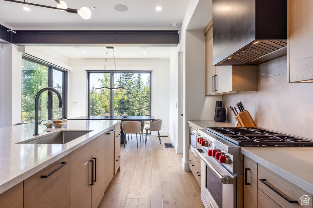 Kitchen featuring luxury range, sink, hanging light fixtures, wall chimney exhaust hood, and light wood-type flooring