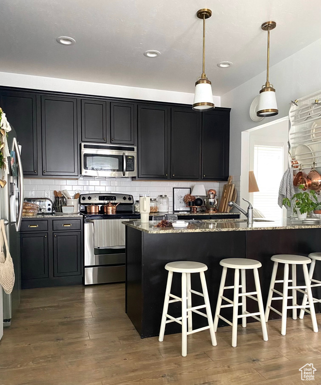 Kitchen with dark hardwood / wood-style floors, a kitchen bar, hanging light fixtures, appliances with stainless steel finishes, and dark stone countertops