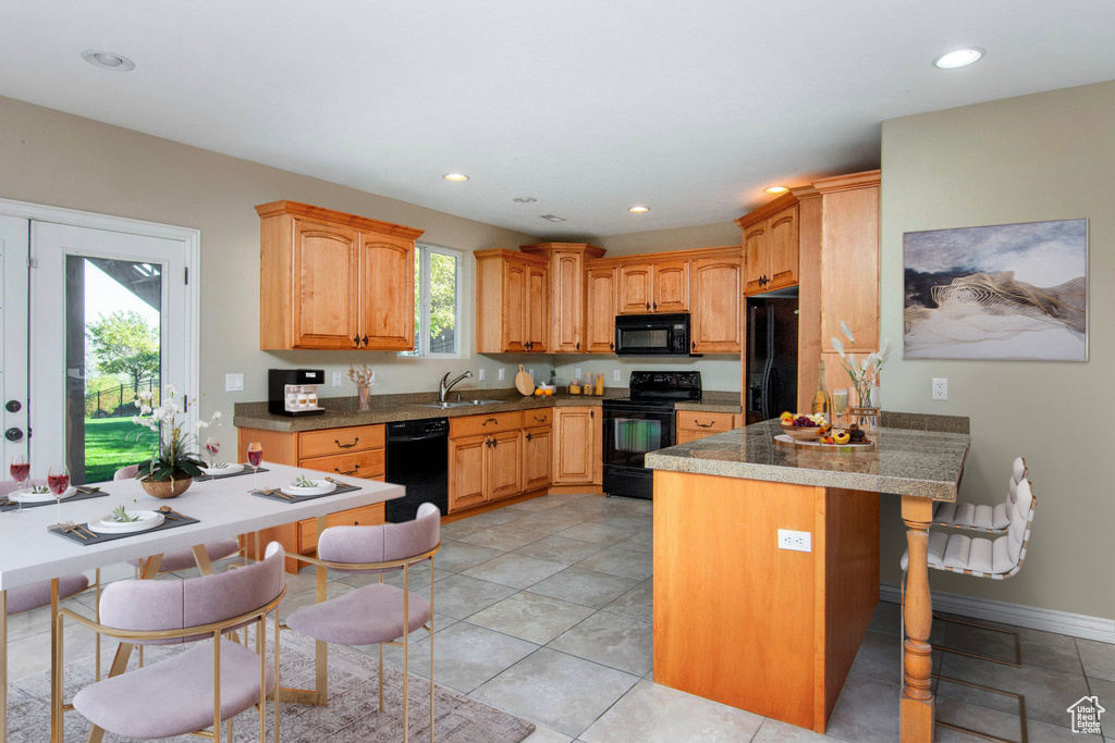 Kitchen featuring kitchen peninsula, a breakfast bar area, light tile patterned floors, black appliances, and sink