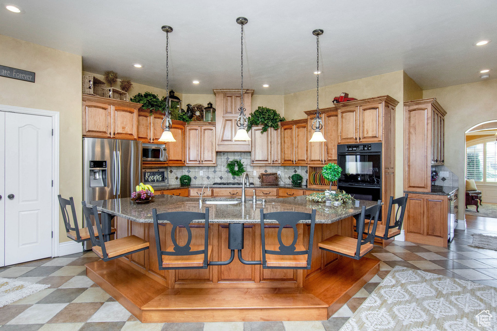 Kitchen featuring a breakfast bar area, an island with sink, hanging light fixtures, stainless steel appliances, and dark stone countertops