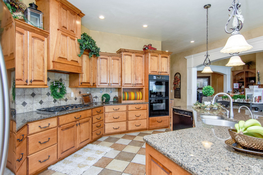 Kitchen with black appliances, backsplash, pendant lighting, and light stone counters