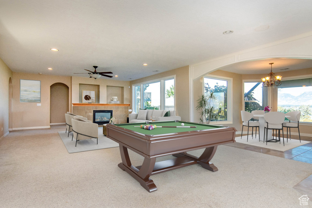 Playroom featuring ceiling fan with notable chandelier, a tile fireplace, light colored carpet, and pool table