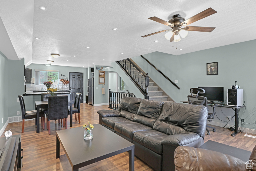 Living room featuring light wood-type flooring, vaulted ceiling, a textured ceiling, and ceiling fan