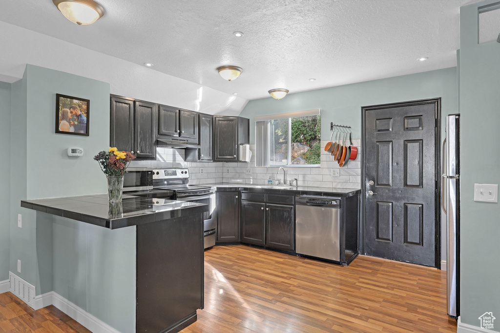 Kitchen featuring appliances with stainless steel finishes, tasteful backsplash, kitchen peninsula, light hardwood / wood-style flooring, and sink