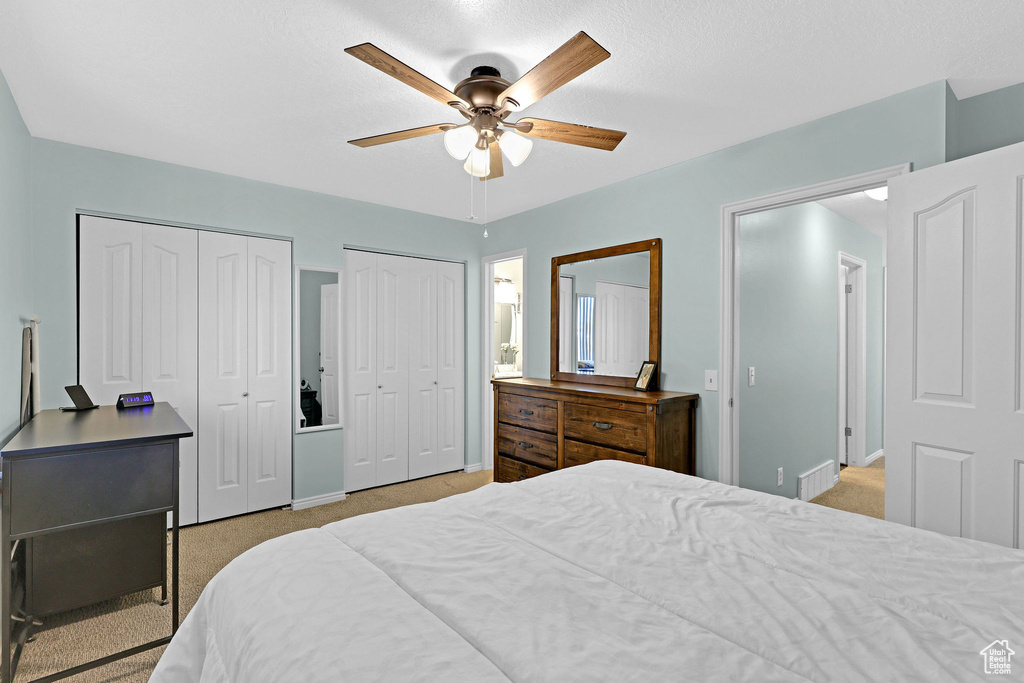 Bedroom with light carpet, a textured ceiling, two closets, and ceiling fan