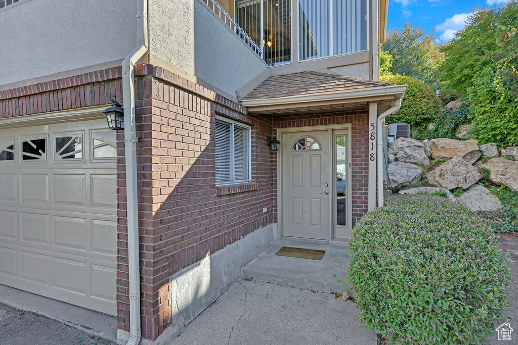 View of exterior entry featuring a balcony, a garage, and central AC