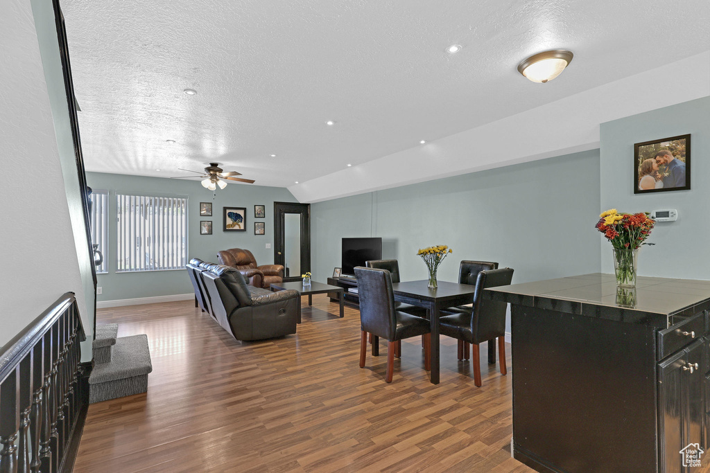 Dining room featuring vaulted ceiling, ceiling fan, dark wood-type flooring, and a textured ceiling