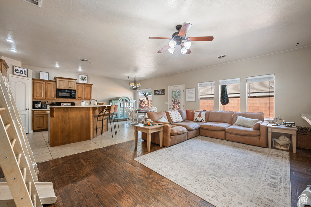 Living room with ceiling fan with notable chandelier and light wood-type flooring