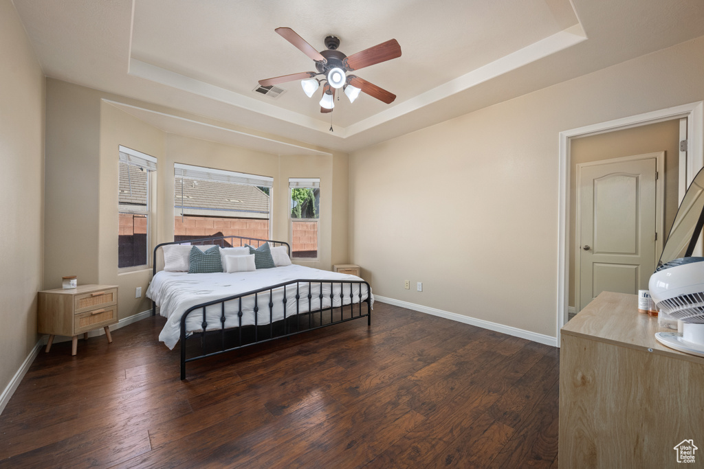 Bedroom with ceiling fan, a tray ceiling, and dark hardwood / wood-style flooring