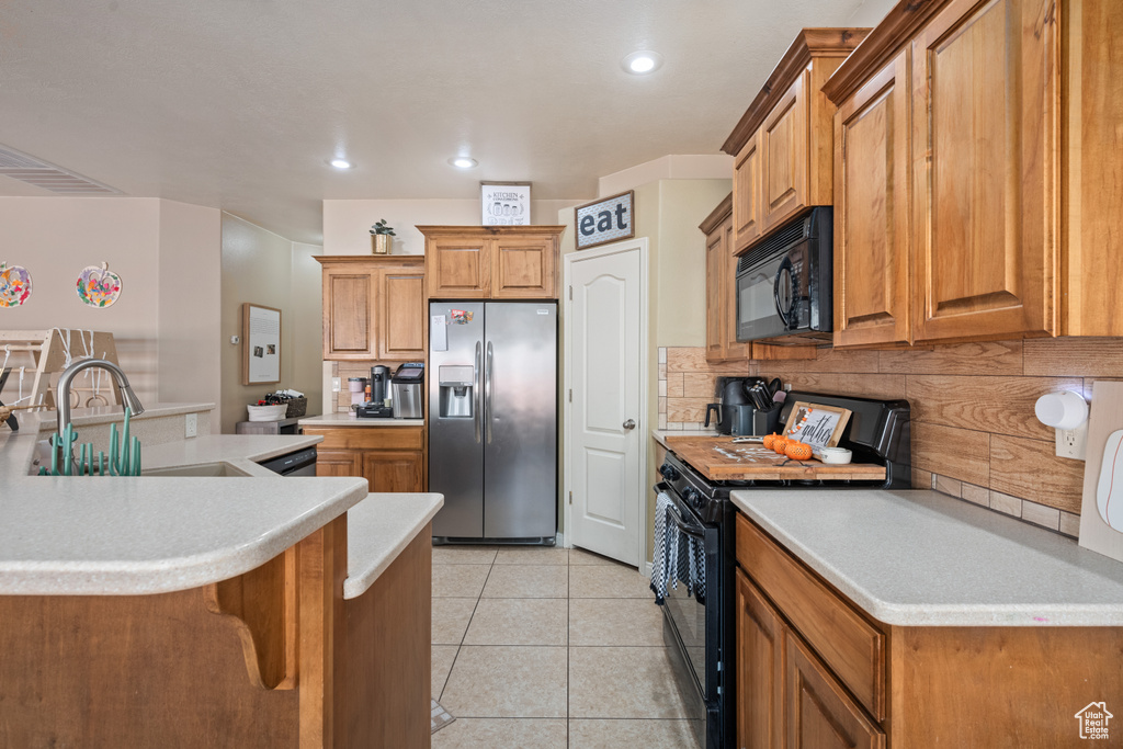 Kitchen featuring light tile patterned floors, sink, tasteful backsplash, black appliances, and a kitchen breakfast bar