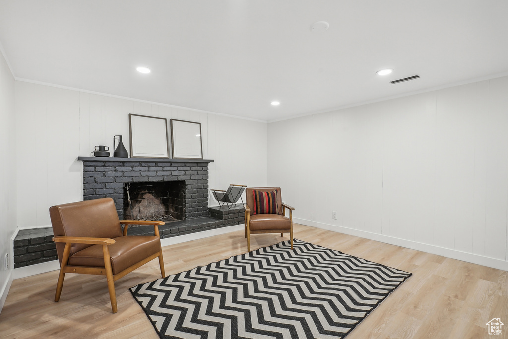 Sitting room featuring light wood-type flooring, a fireplace, and crown molding