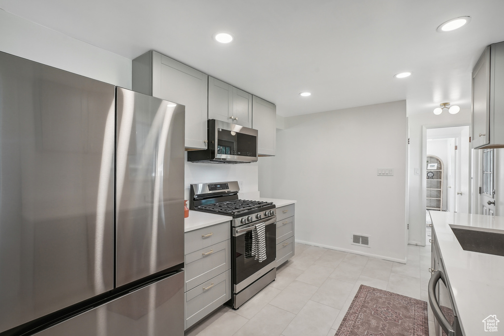 Kitchen with gray cabinets, appliances with stainless steel finishes, and light tile patterned floors